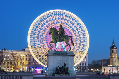 Equestrian statue of Louis XIV located in Place Bellecour with a Ferris Wheel in the background at night in Lyon, France
