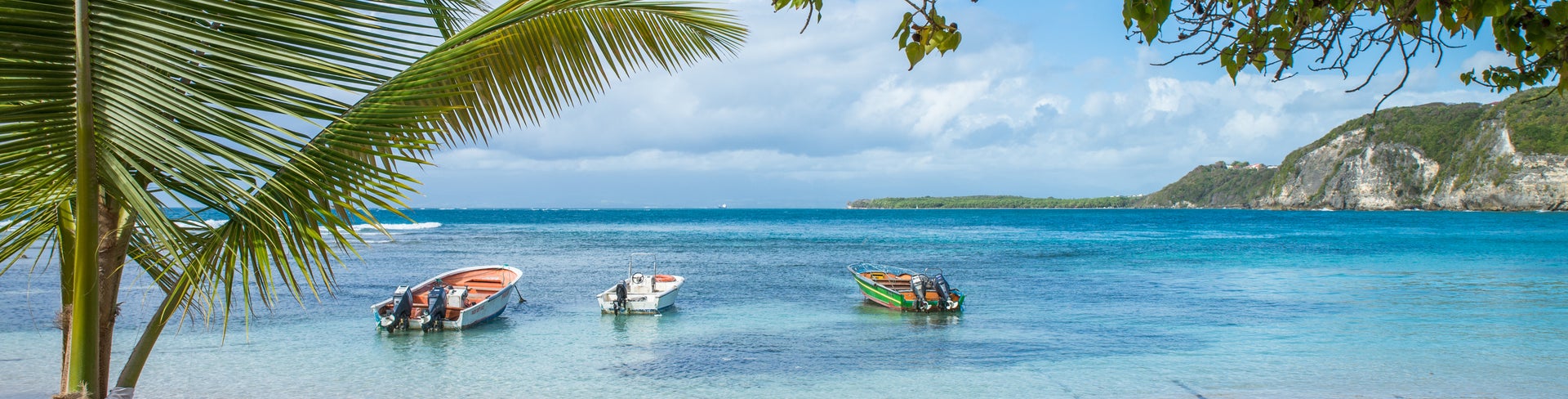 Plage de Petit Havre in Le Gosier, Guadeloupe, features a tranquil beach with soft white sand, turquoise waters, and lush palm trees