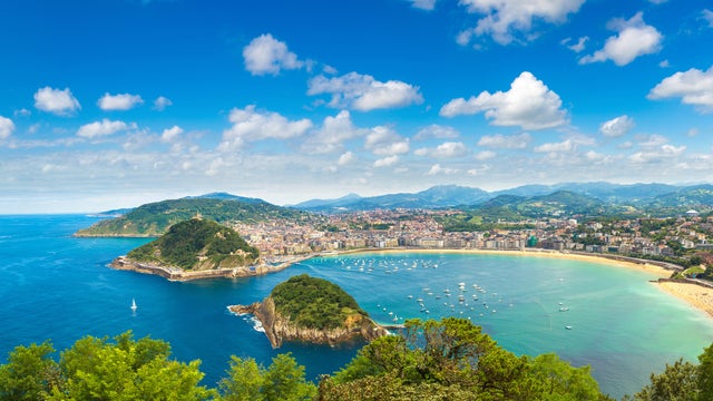 Panoramic view of San Sebastián, Spain, featuring La Concha Bay, golden sandy beaches, lush green hills, and the charming cityscape along the coastline