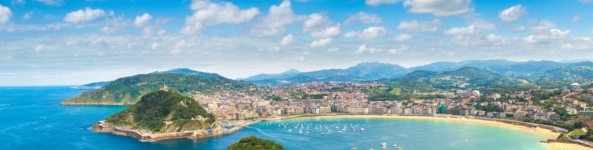 Panoramic view of San Sebastián, Spain, featuring La Concha Bay, golden sandy beaches, lush green hills, and the charming cityscape along the coastline