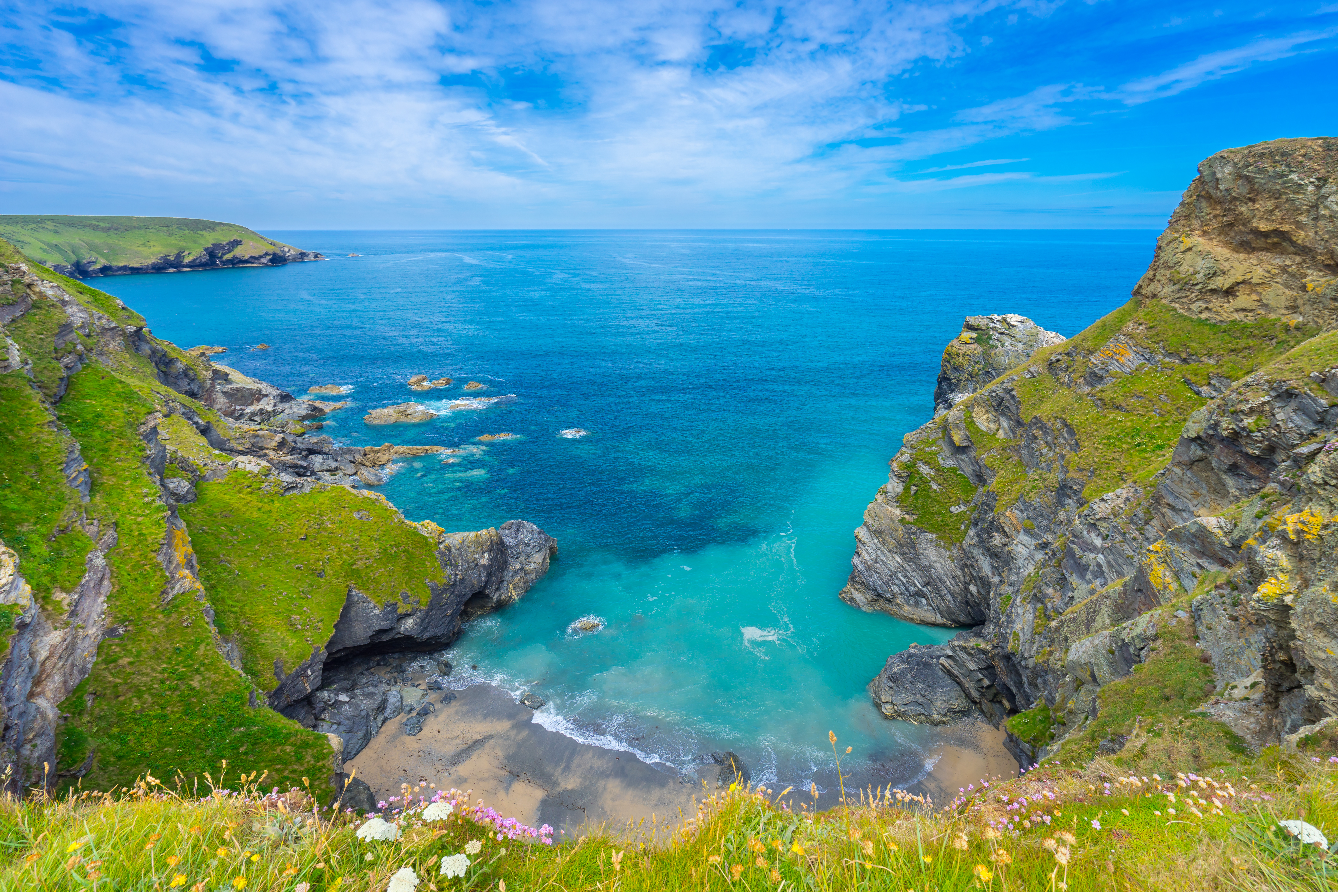 Aerial view of the ocean surrounded by dramatic cliffs along the coastline of Devon, United Kingdom, with waves crashing at the base and lush green landscape above