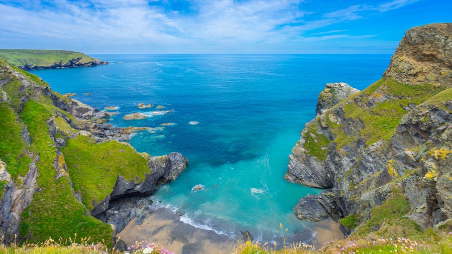 Aerial view of the ocean surrounded by dramatic cliffs along the coastline of Devon, United Kingdom, with waves crashing at the base and lush green landscape above