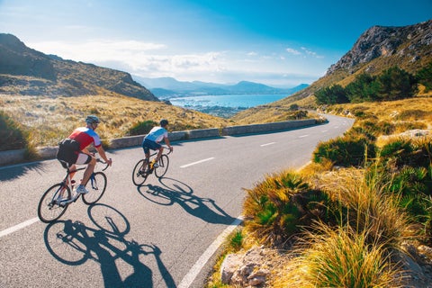 Bikers riding along a scenic road in Palma de Mallorca, Spain, with the Serra de Tramuntana mountains in the background