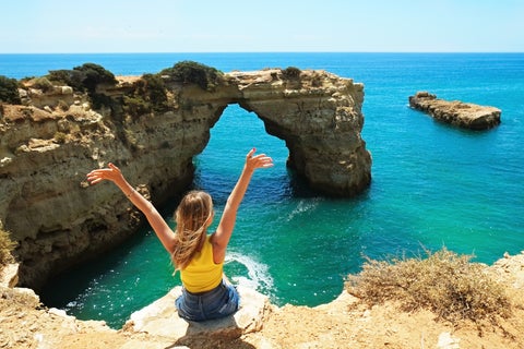 Tourist posing for a picture with the rock formations of the Algarve coast at a beach near Faro, Portugal