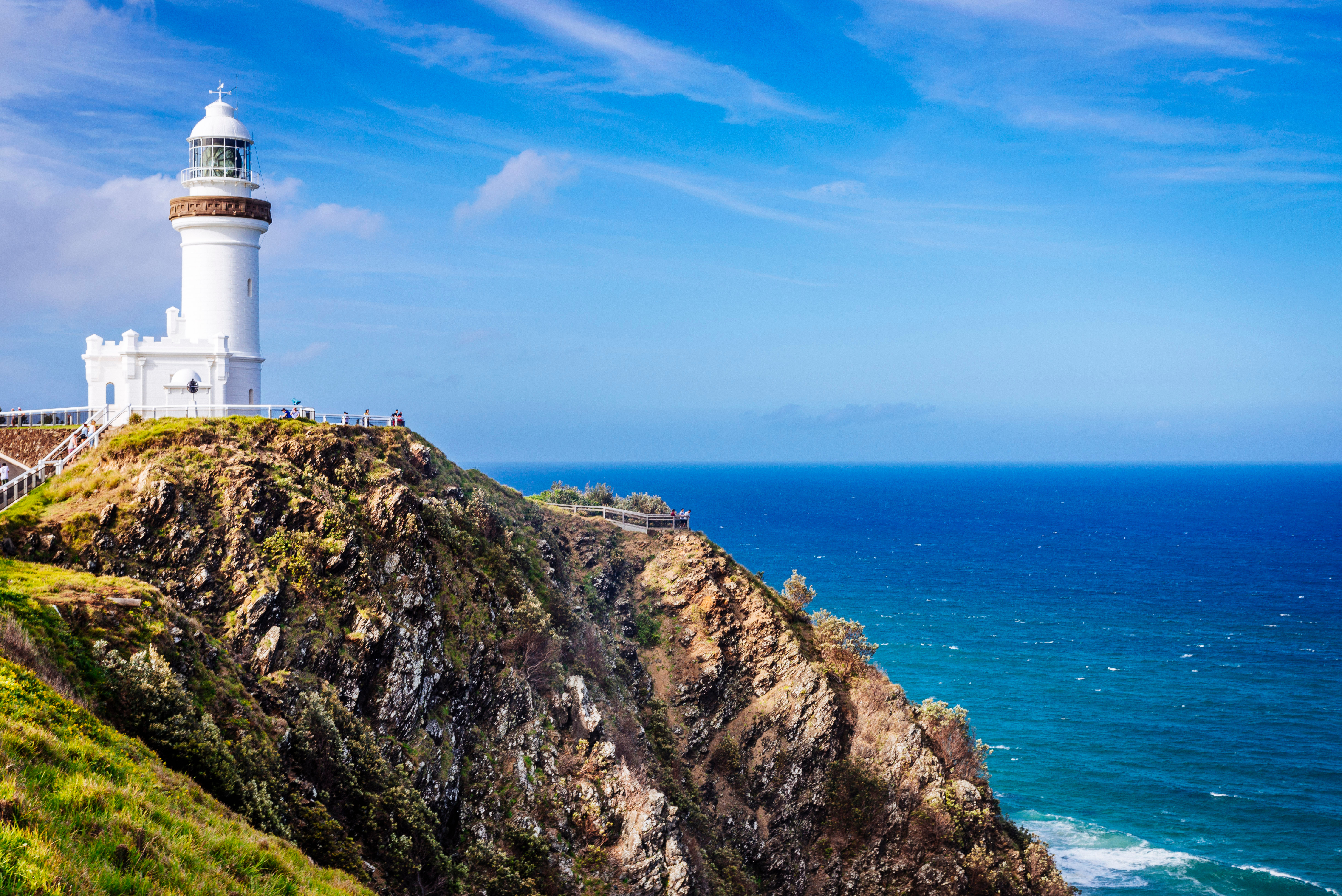 Byron Bay Lighthouse with an iconic white structure perched atop a rugged cliff, surrounded by lush greenery and overlooking the turquoise waters of the Pacific Ocean