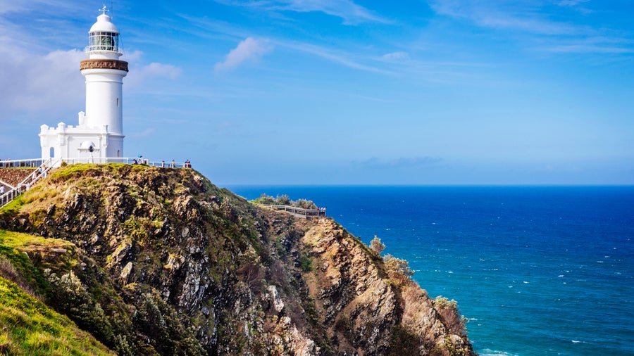 Byron Bay Lighthouse with an iconic white structure perched atop a rugged cliff, surrounded by lush greenery and overlooking the turquoise waters of the Pacific Ocean