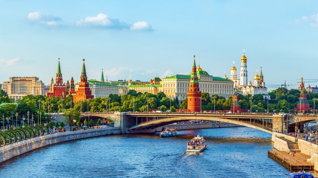 Boat on the Moskva River passing under the Bolshoy Kamenny Bridge, with colorful domes of St. Basil's Cathedral, the historic GUM Department Store, and the Moscow Kremlin in the background