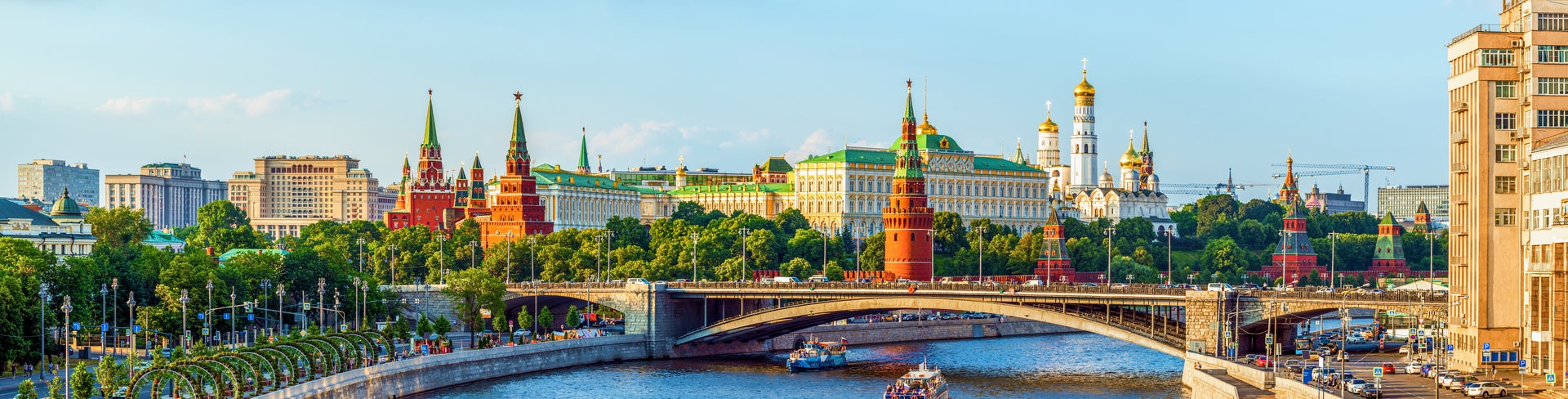 Boat on the Moskva River passing under the Bolshoy Kamenny Bridge, with colorful domes of St. Basil's Cathedral, the historic GUM Department Store, and the Moscow Kremlin in the background