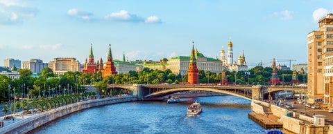 Boat on the Moskva River passing under the Bolshoy Kamenny Bridge, with colorful domes of St. Basil's Cathedral, the historic GUM Department Store, and the Moscow Kremlin in the background