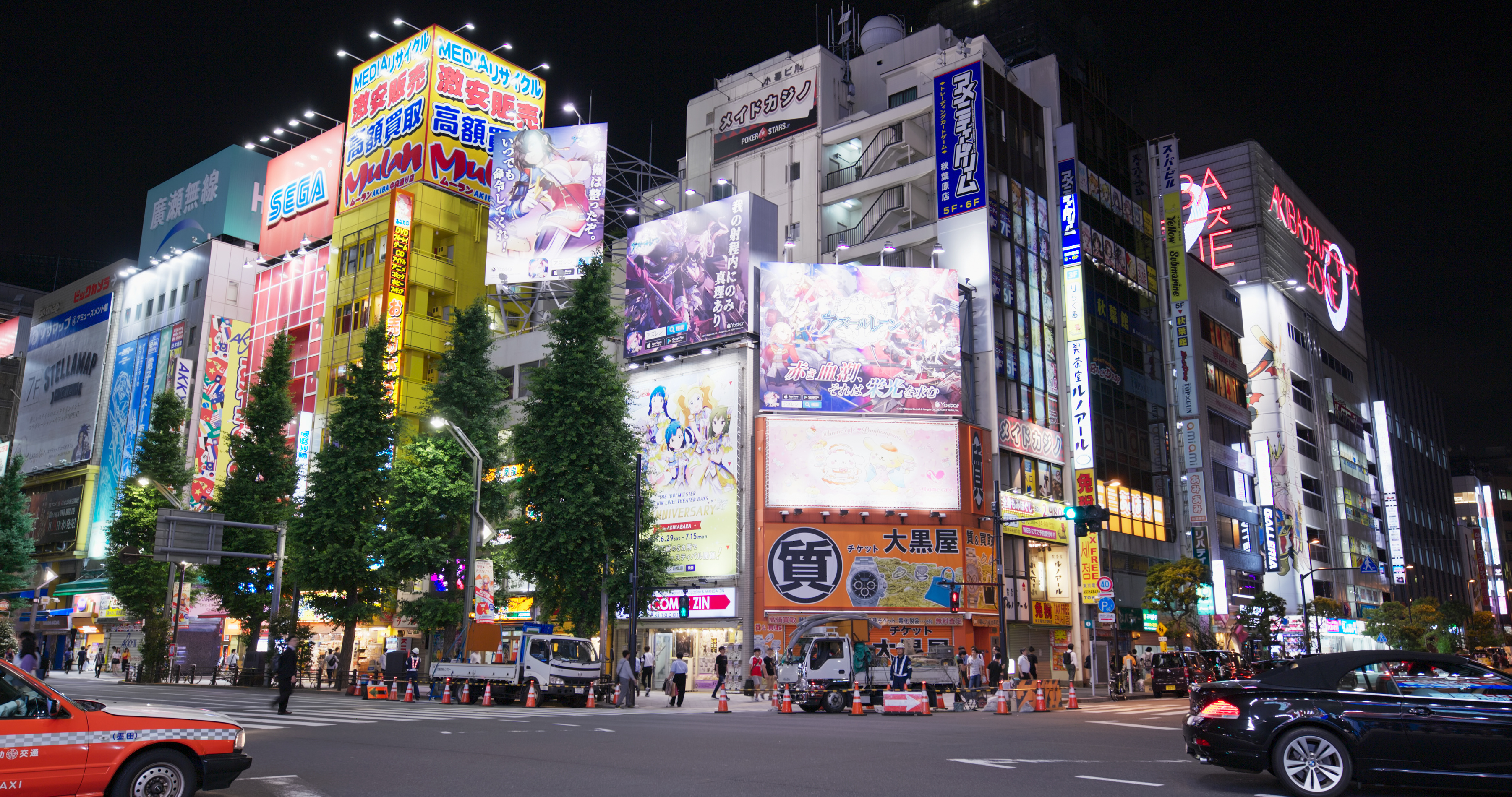 A nighttime aerial view of Tokyo's Akihabara with its vibrant, illuminated cityscape bursting with colorful neon signs and digital billboards