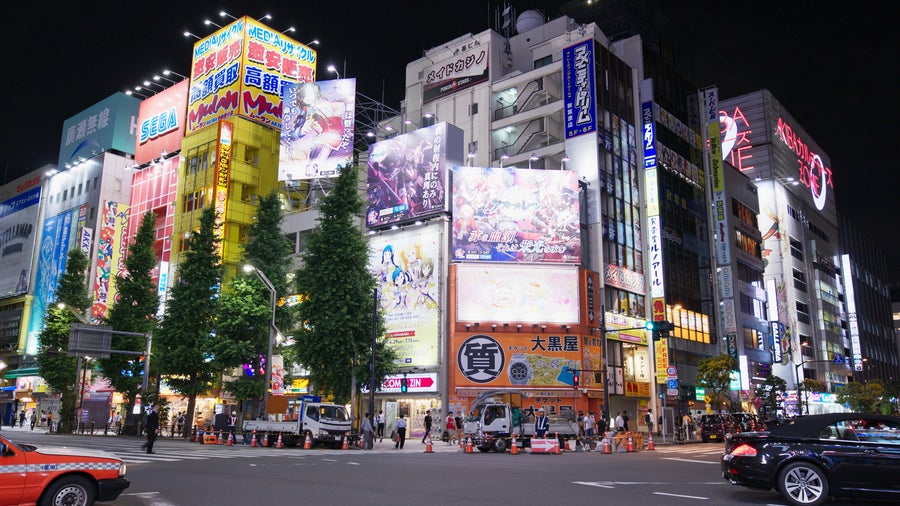 A nighttime aerial view of Tokyo's Akihabara with its vibrant, illuminated cityscape bursting with colorful neon signs and digital billboards