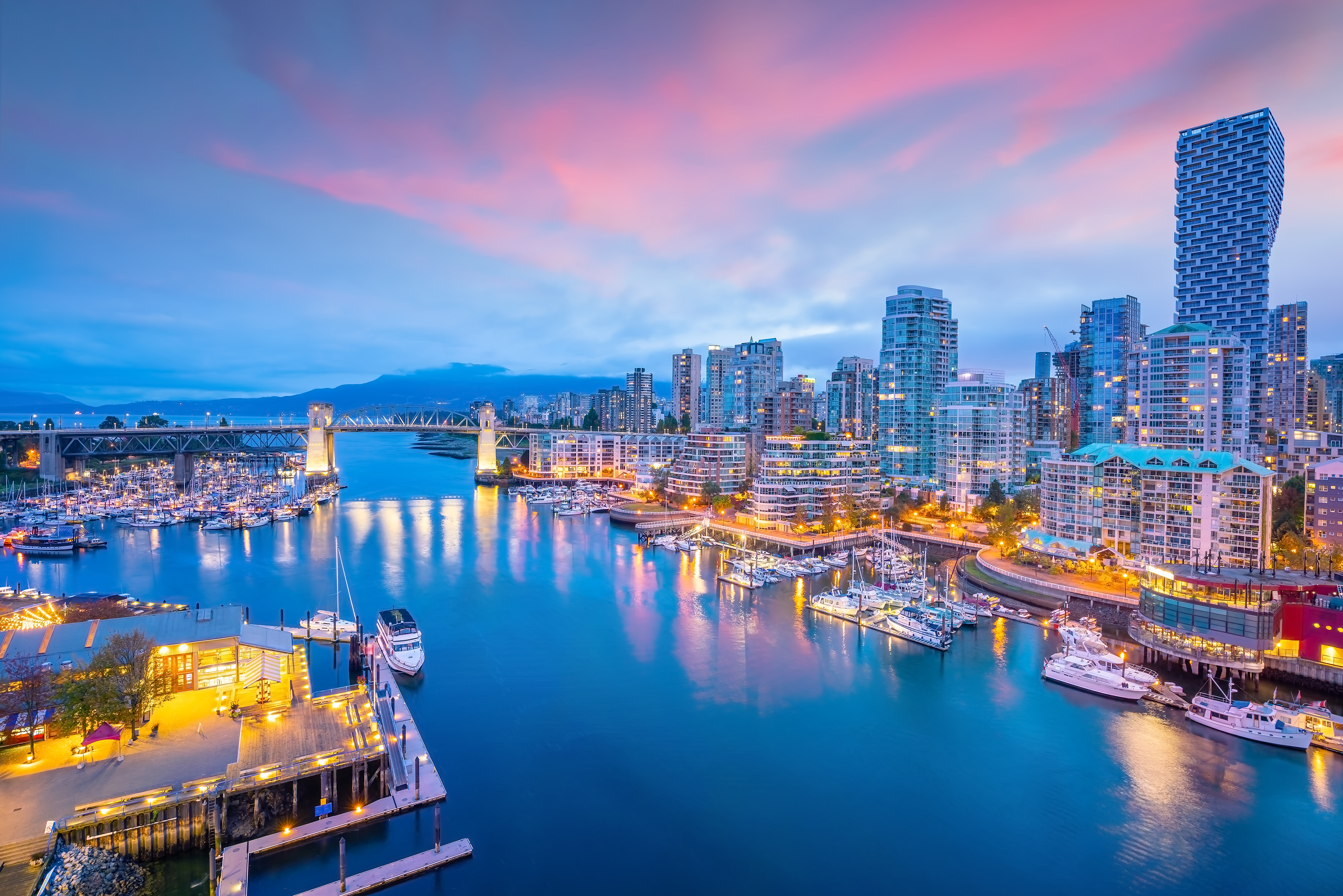 Vancouver skyline at sunset with a pink sky, modern bridge and river reflections along the waterfront