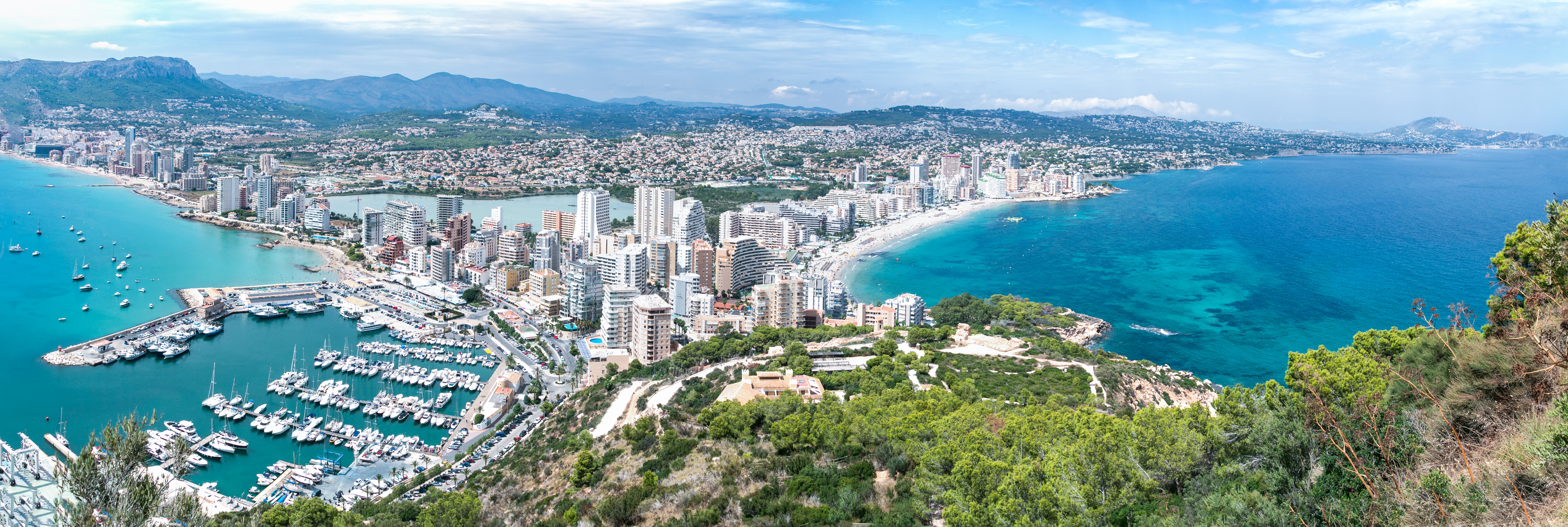 Panoramic aerial view of the coastline at Calpe, Spain, showcasing the Mediterranean Sea, sandy beaches, and the iconic Peñón de Ifach rock formation