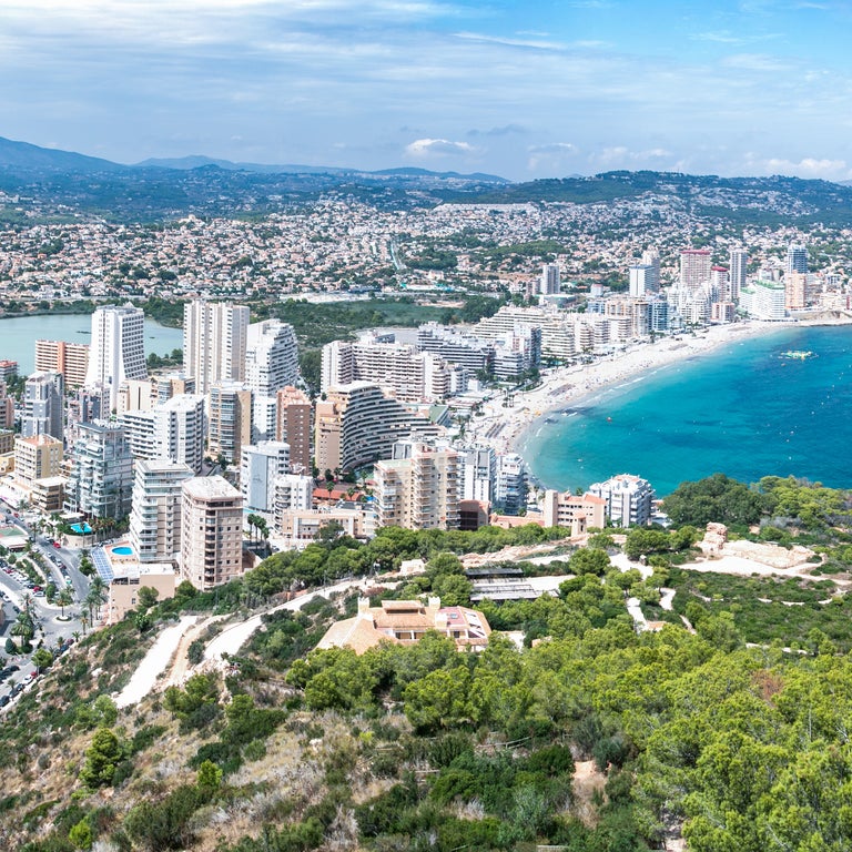 Panoramic aerial view of the coastline at Calpe, Spain, showcasing the Mediterranean Sea, sandy beaches, and the iconic Peñón de Ifach rock formation