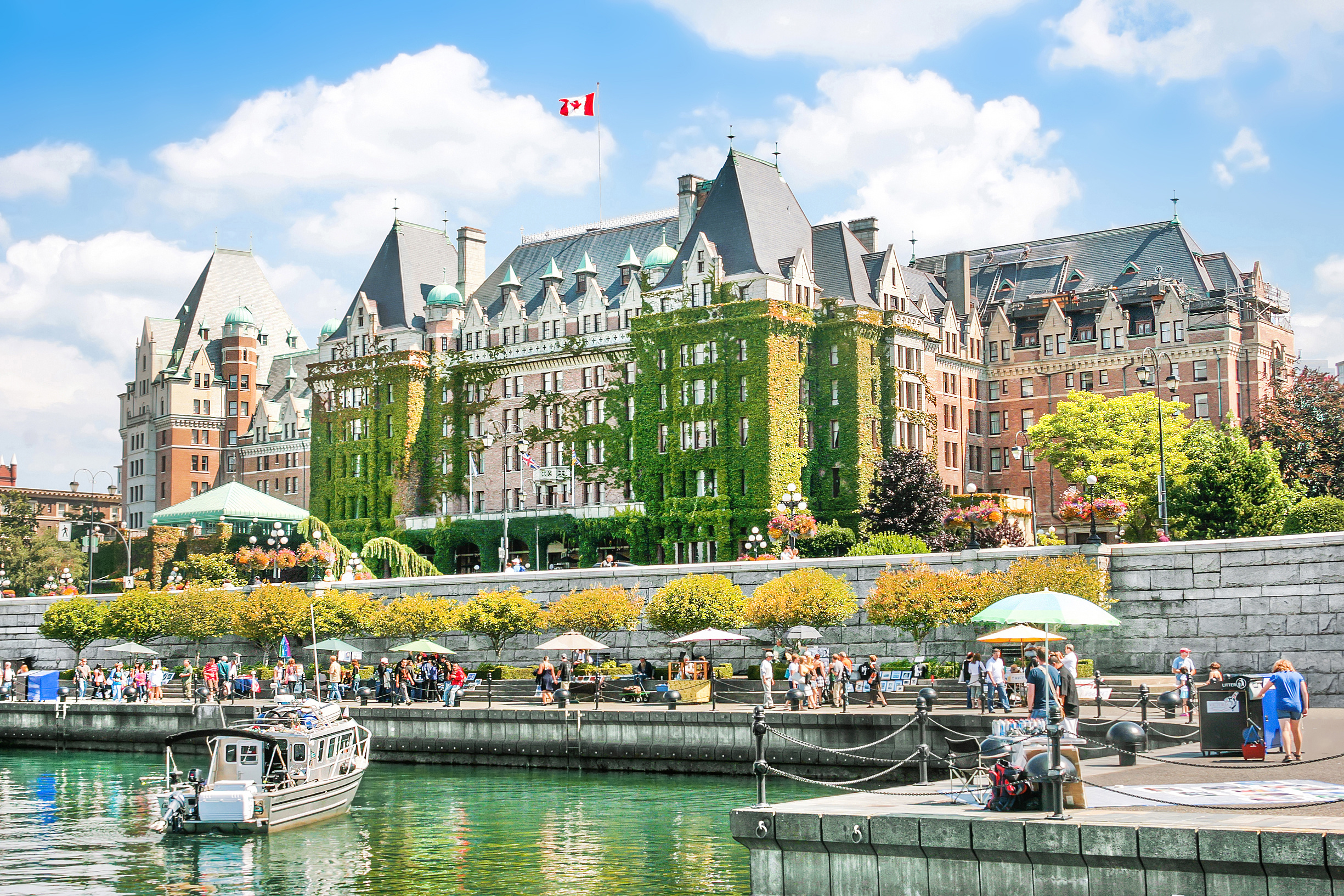 Sailboats and small ferries float on the calm, reflective waters, surrounded by the vibrant architecture of historic buildings and modern establishments in Inner Harbour in Victoria, British Columbia, Canada