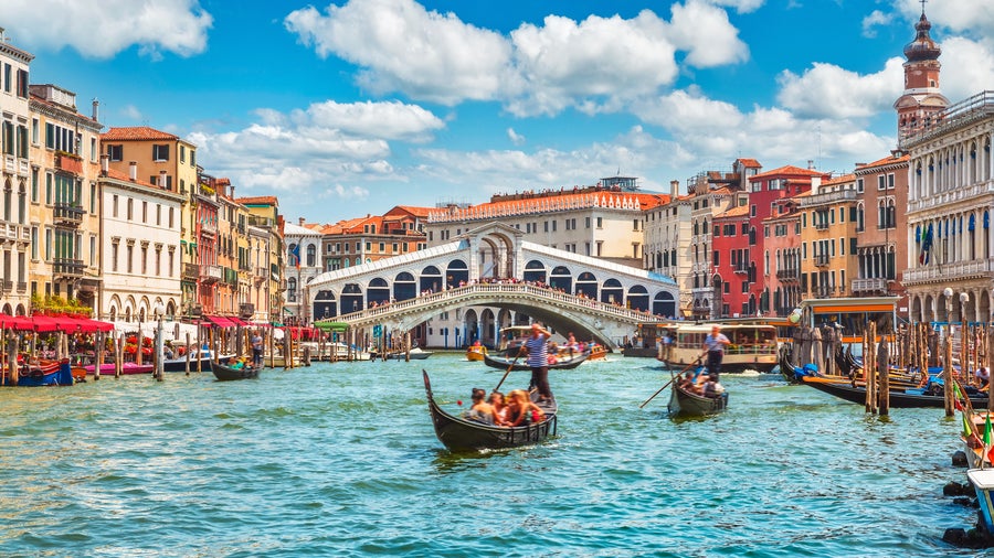Traditional flat-bottomed gondola boat gliding through Venice canals with a historic bridge in the background