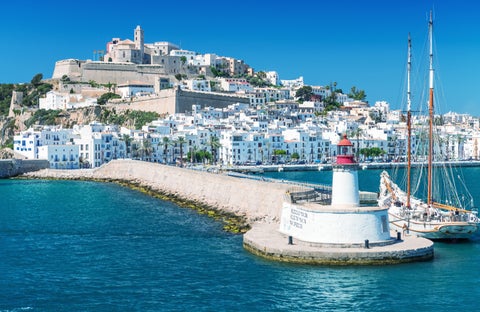 View from the coast of Ibiza, Spain showing a path leading to Talamanca Beach, with the lighthouse at Punta Grossa and white houses in the background