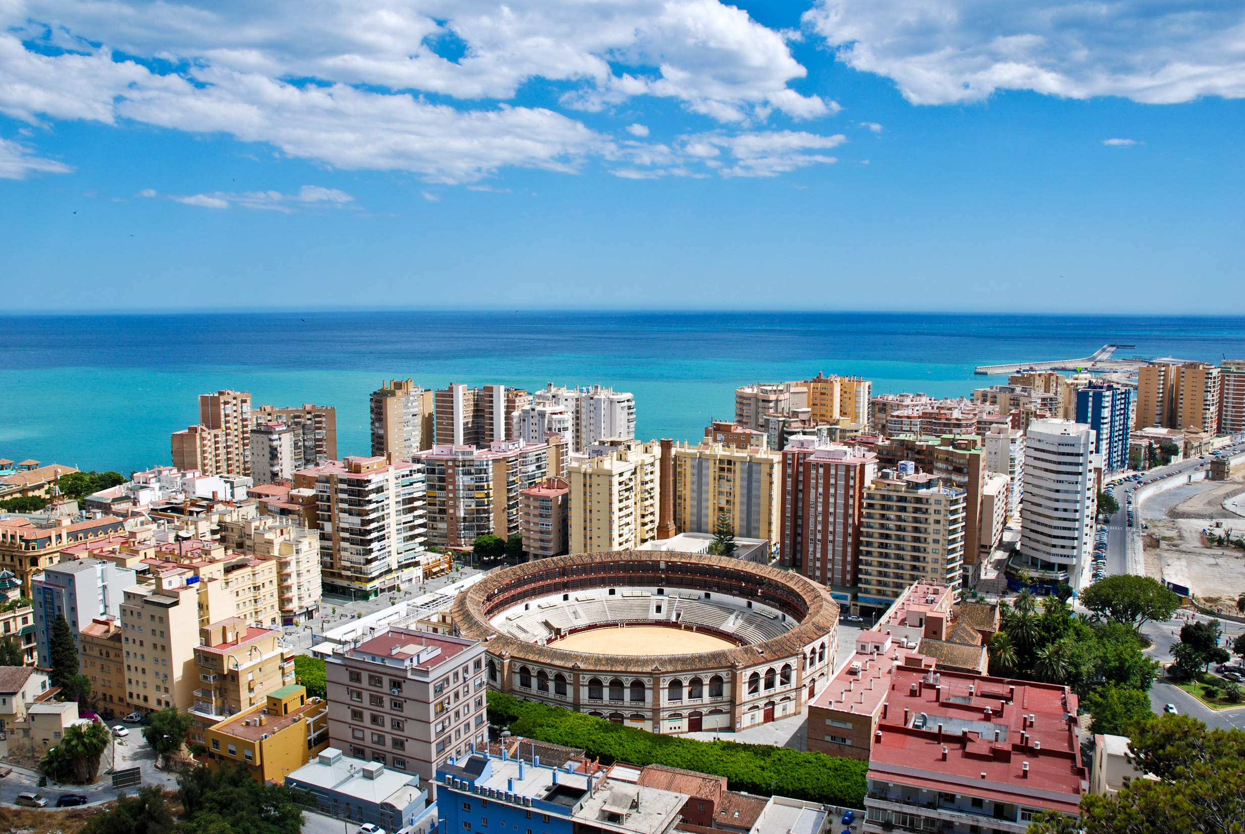 Aerial view of Málaga, Andalusia, Spain, featuring the historic Alcazaba fortress, busy port, sandy beaches, Mediterranean Sea, and hills in the background