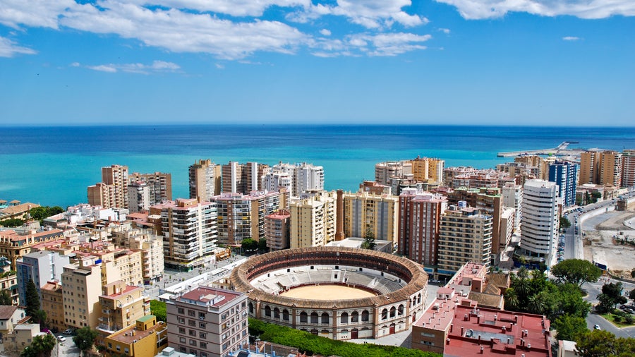 Aerial view of Málaga, Andalusia, Spain, featuring the historic Alcazaba fortress, busy port, sandy beaches, Mediterranean Sea, and hills in the background