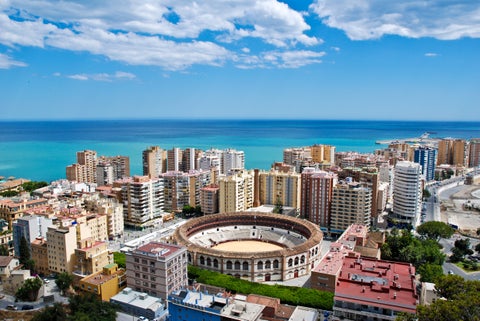 Aerial view of Málaga, Andalusia, Spain, featuring the historic Alcazaba fortress, busy port, sandy beaches, Mediterranean Sea, and hills in the background