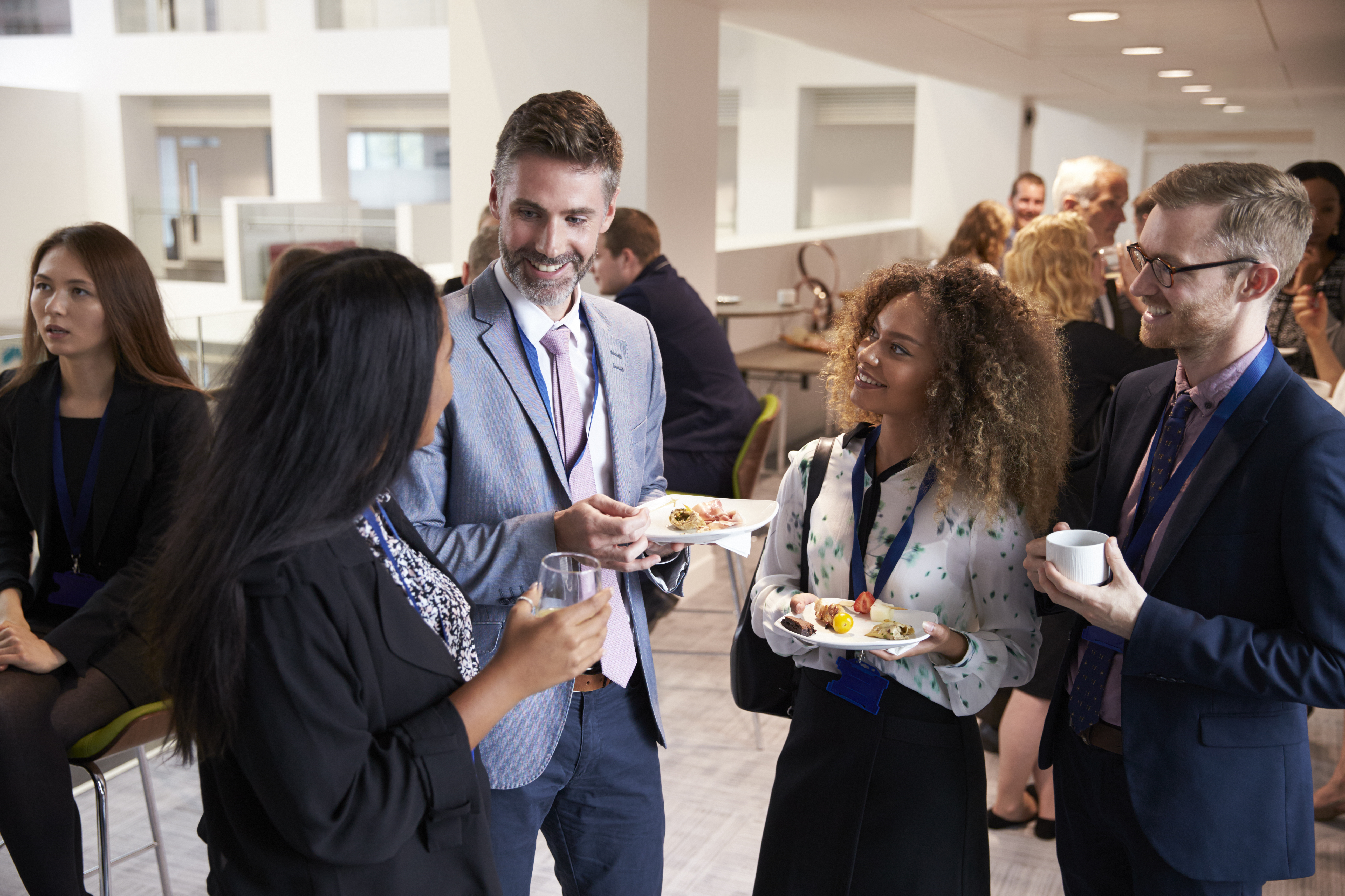 Coworkers interacting at a corporate event while holding plates with food and drinks