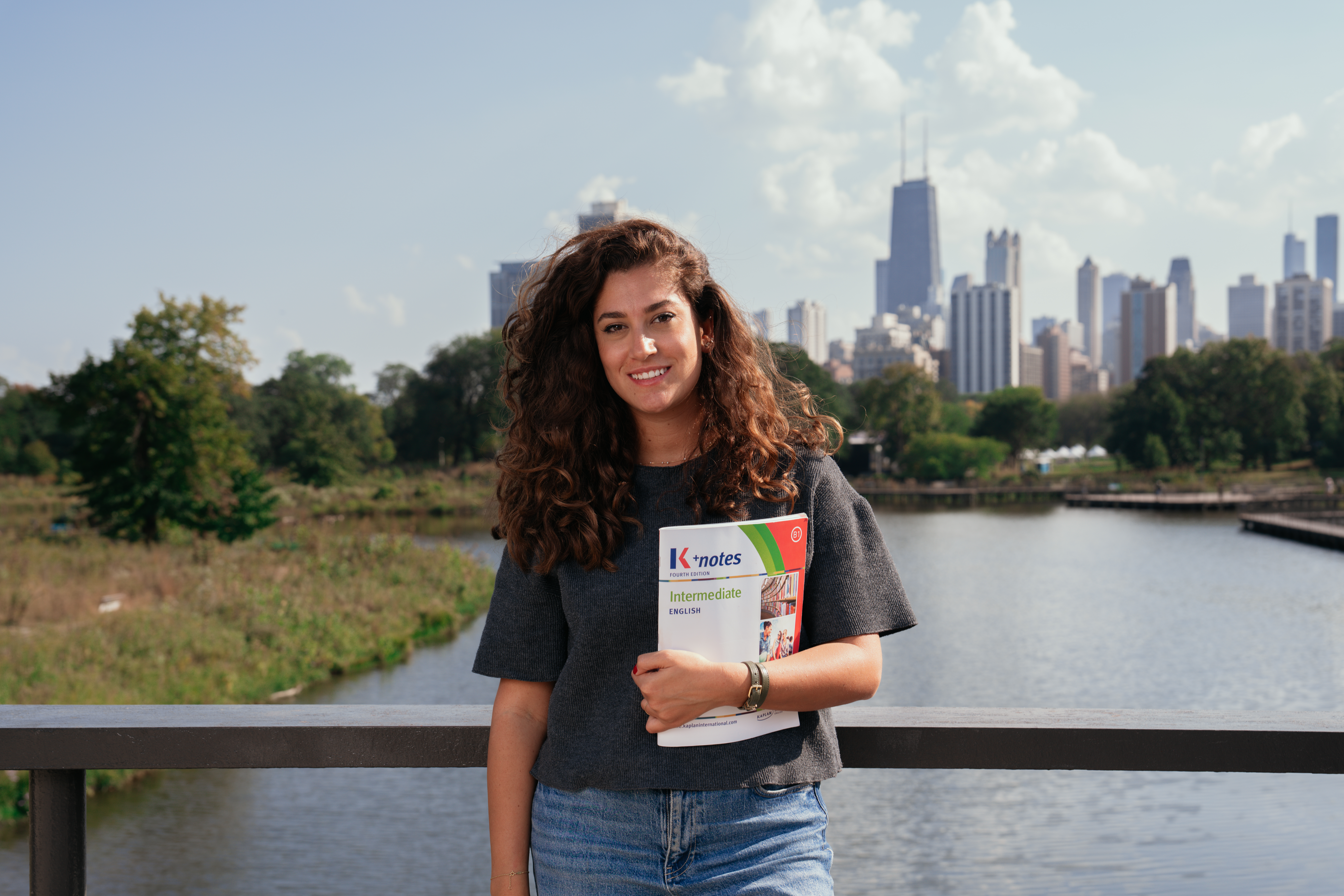 Female student holding a Kaplan folder, posing in a Chicago park by Lake Michigan