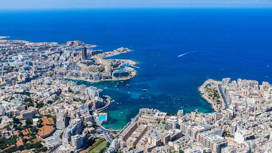 Aerial view of Malta showing St. Julian’s and Tas-Sliema, with St. Julian’s Bay, Balluta Bay, and Spinola Bay, along with harbours, coastline, and the Paceville skyscraper in the background