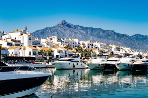 Boats at Puerto de Málaga with white houses along the waterfront and the Montes de Málaga mountains in the background