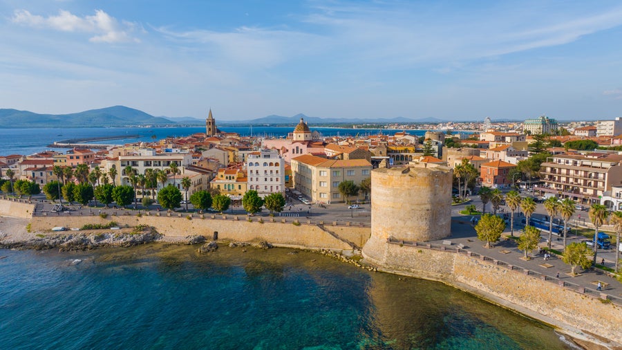 Aerial view of Alghero, Italy, showing the seafront and historic buildings along the coast