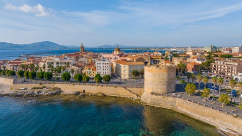 Aerial view of Alghero, Italy, showing the seafront and historic buildings along the coast