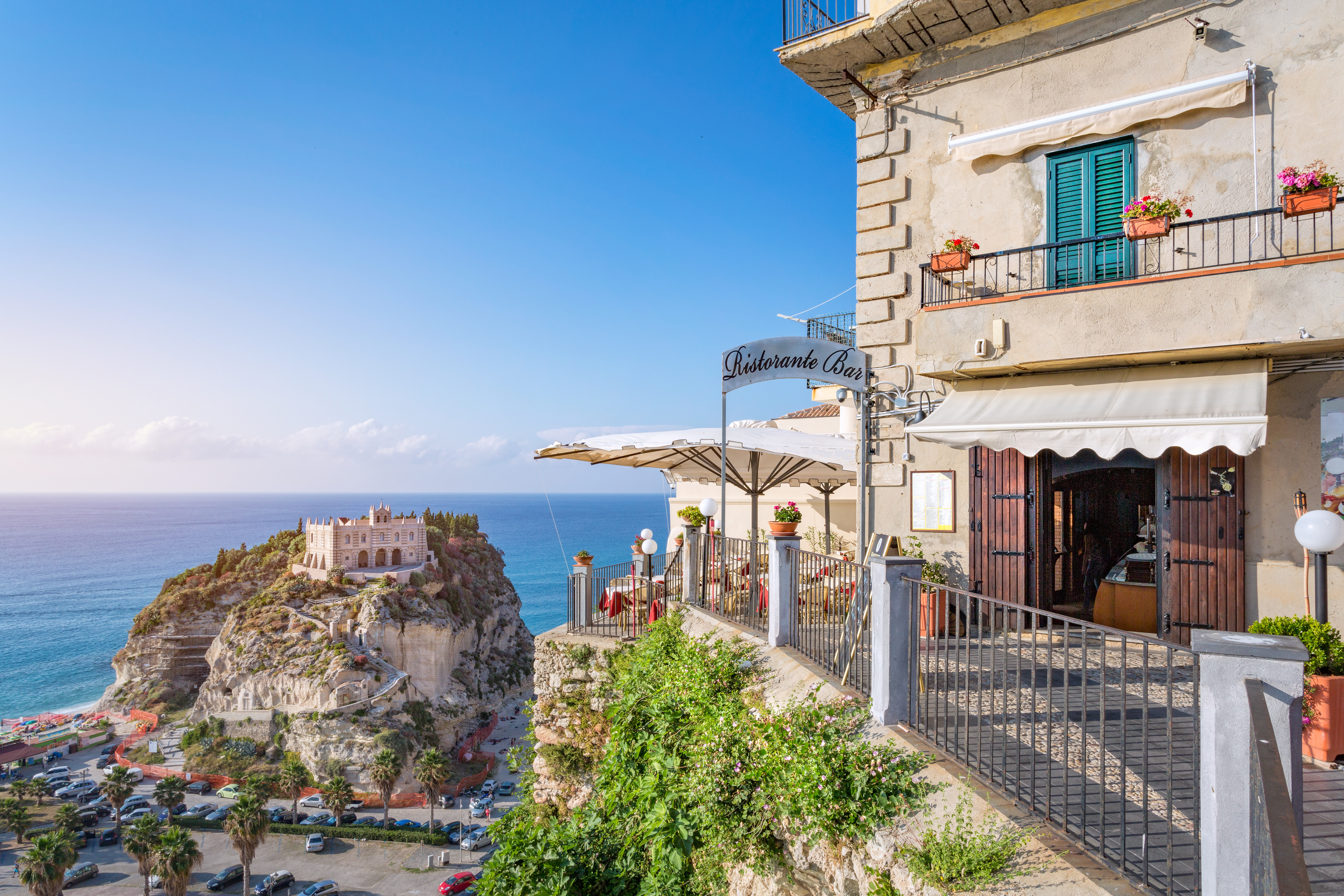 Traditional restaurant with classic balcony with Sanctuary of Santa Maria dell’Isola in the background at Tropea, Italy,