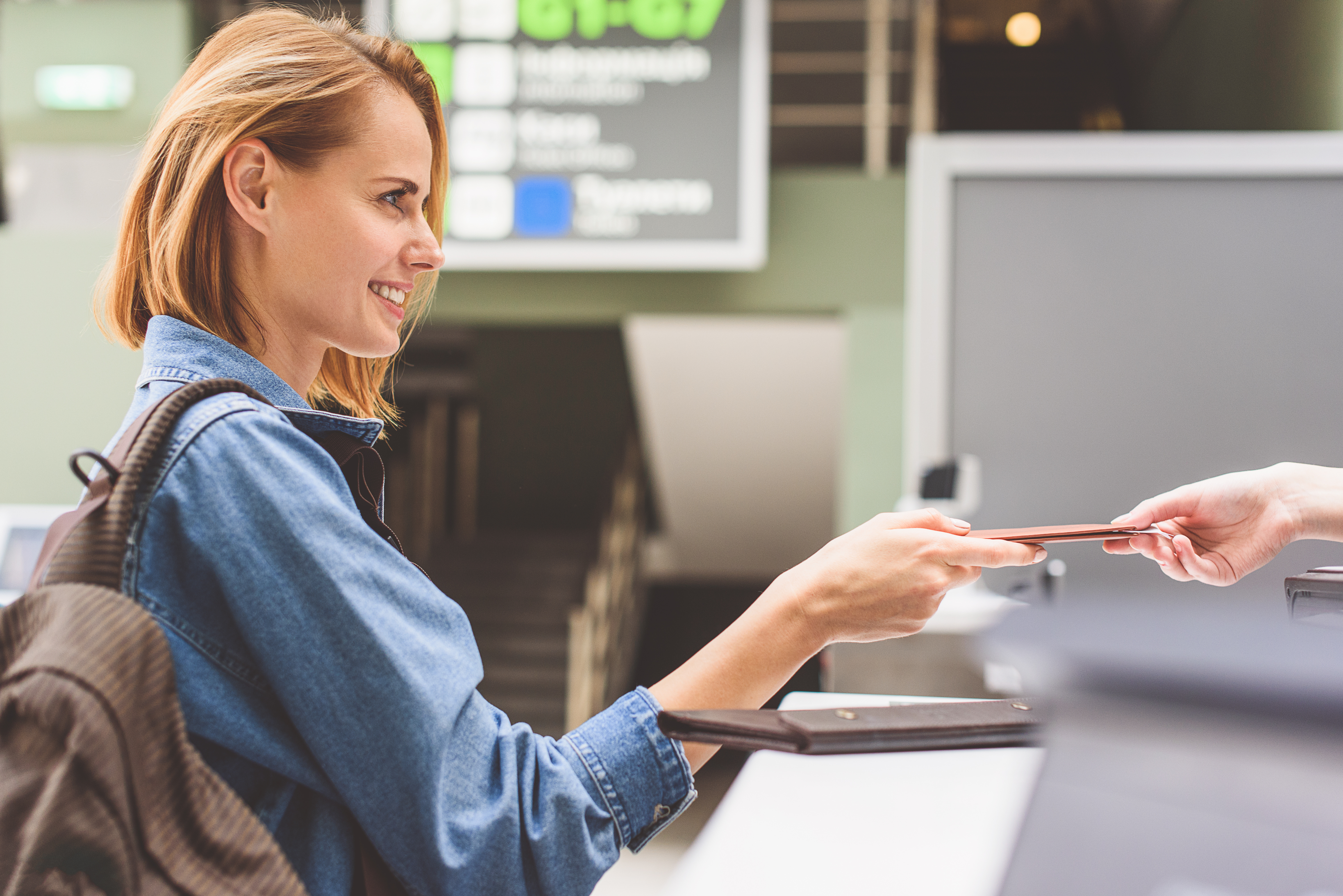 Traveler girl at the airport check-in counter smiling while receiving her passport back