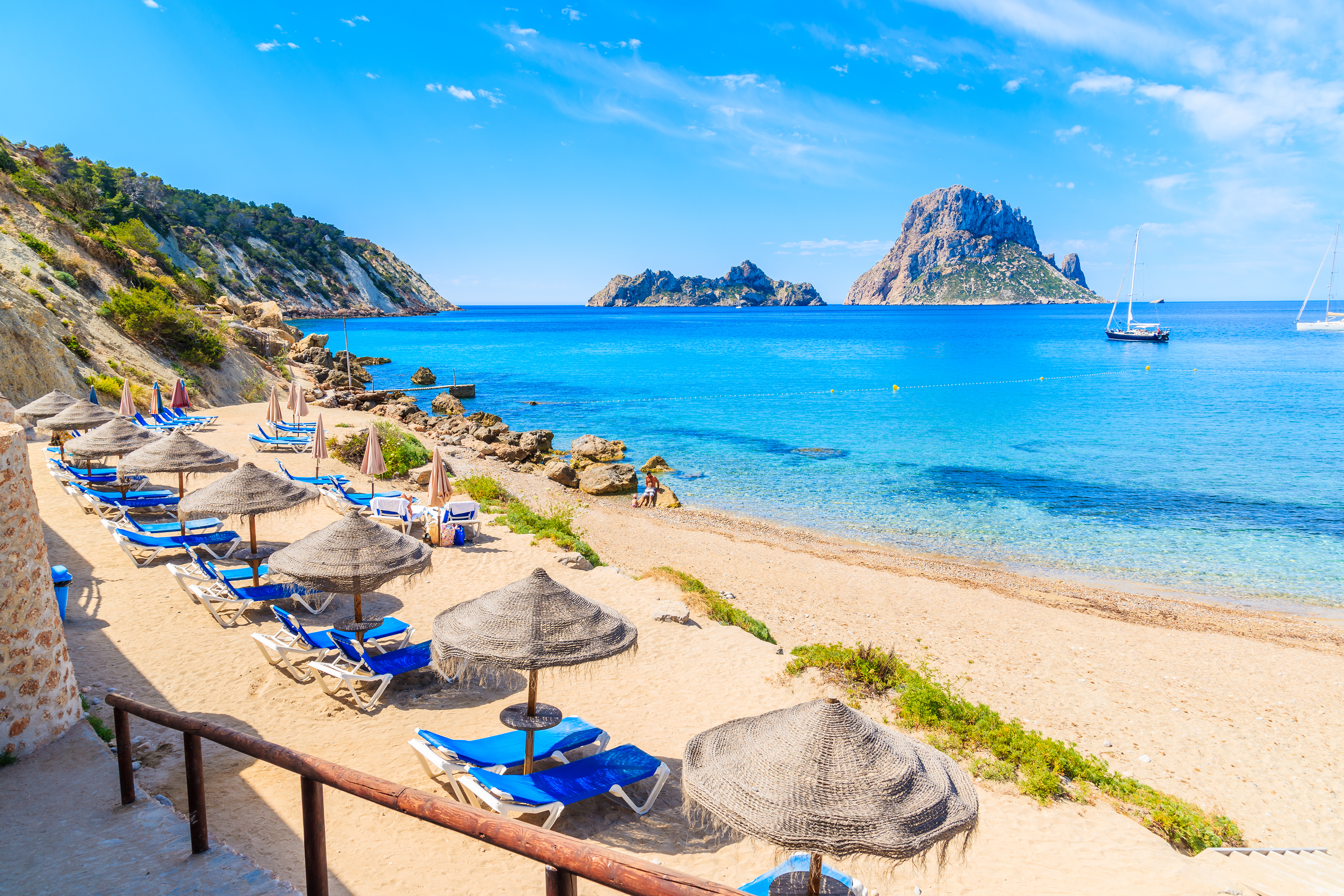 Beach at Ibiza, Spain with colorful umbrellas and beach chairs, crystal clear sea, and boats in the water