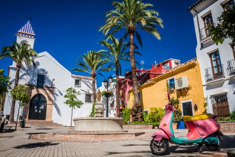 Colourful Vespa scooter in the city center of Marbella, Spain, with the white facade of Iglesia de Nuestra Señora de la Encarnación church in the background