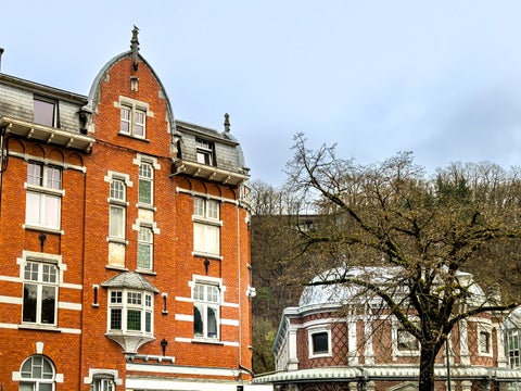 Belle‑Époque villa with orange‑toned brick façade, bow windows, and decorative stone trim on a leafy boulevard in the historic centre of Spa, Belgium