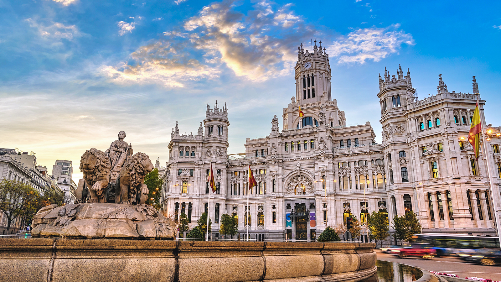 The majestic Cybele Palace, featuring its intricate white stone facade and towers, stands behind the iconic Cibeles Fountain in Madrid, Spain, at sunset, representing the historical and cultural richness encountered during language study abroad programs.