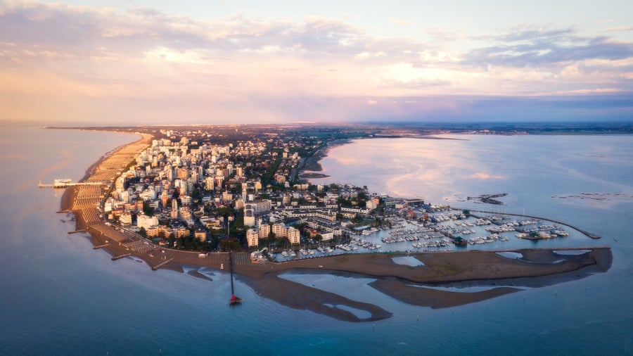 "Aerial view of Lignano, Italy, showing its coastline, beaches, and green urban areas