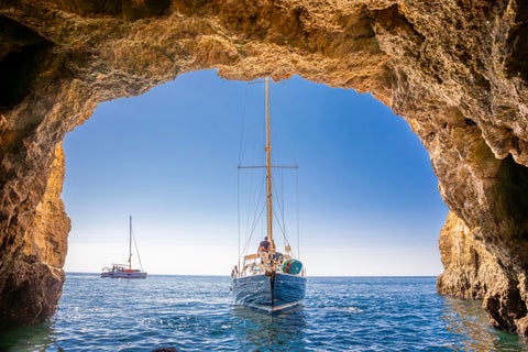 Boat crossing near the limestone rock formations of the Algarve coast at a beach near Faro, Portugal