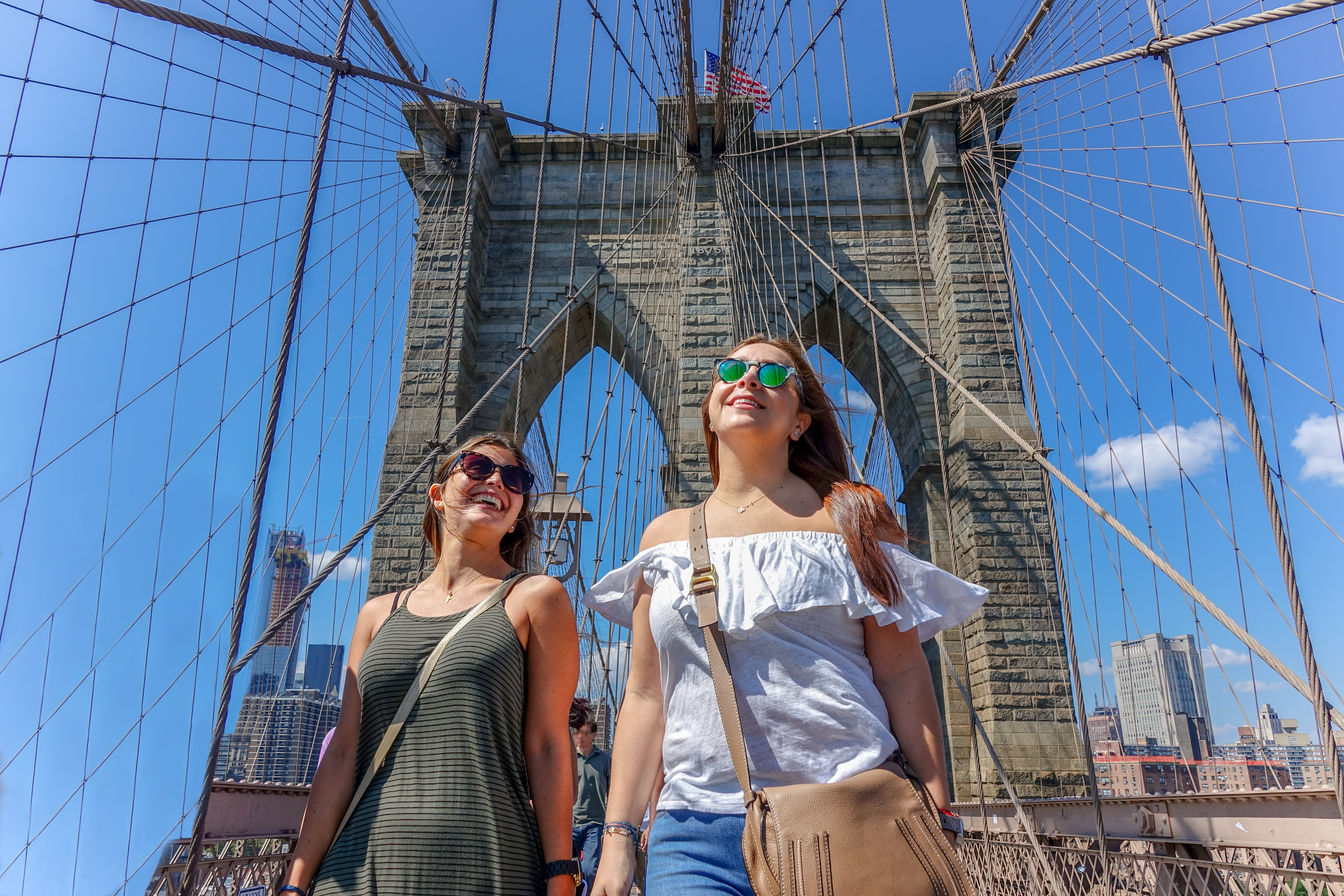 Tourist girls walking inside Brooklyn Bridge with Manhattan skyline in New York City