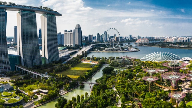 Panoramic aerial view of Singapore City featuring Marina Bay Sands towers, the Singapore Flyer ferris wheel, modern buildings, and the Singapore River