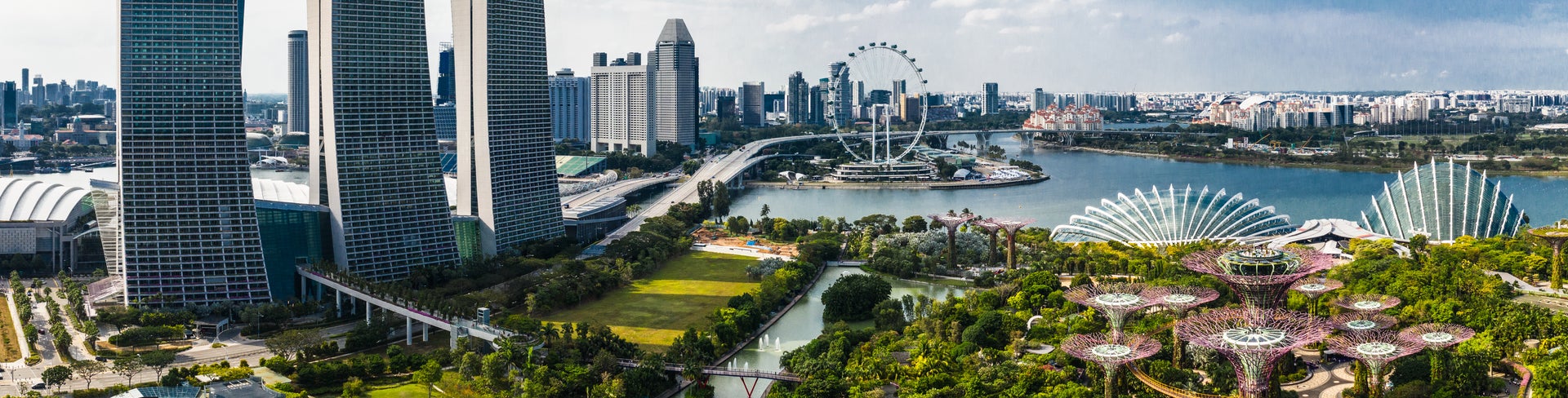 Panoramic aerial view of Singapore City featuring Marina Bay Sands towers, the Singapore Flyer ferris wheel, modern buildings, and the Singapore River