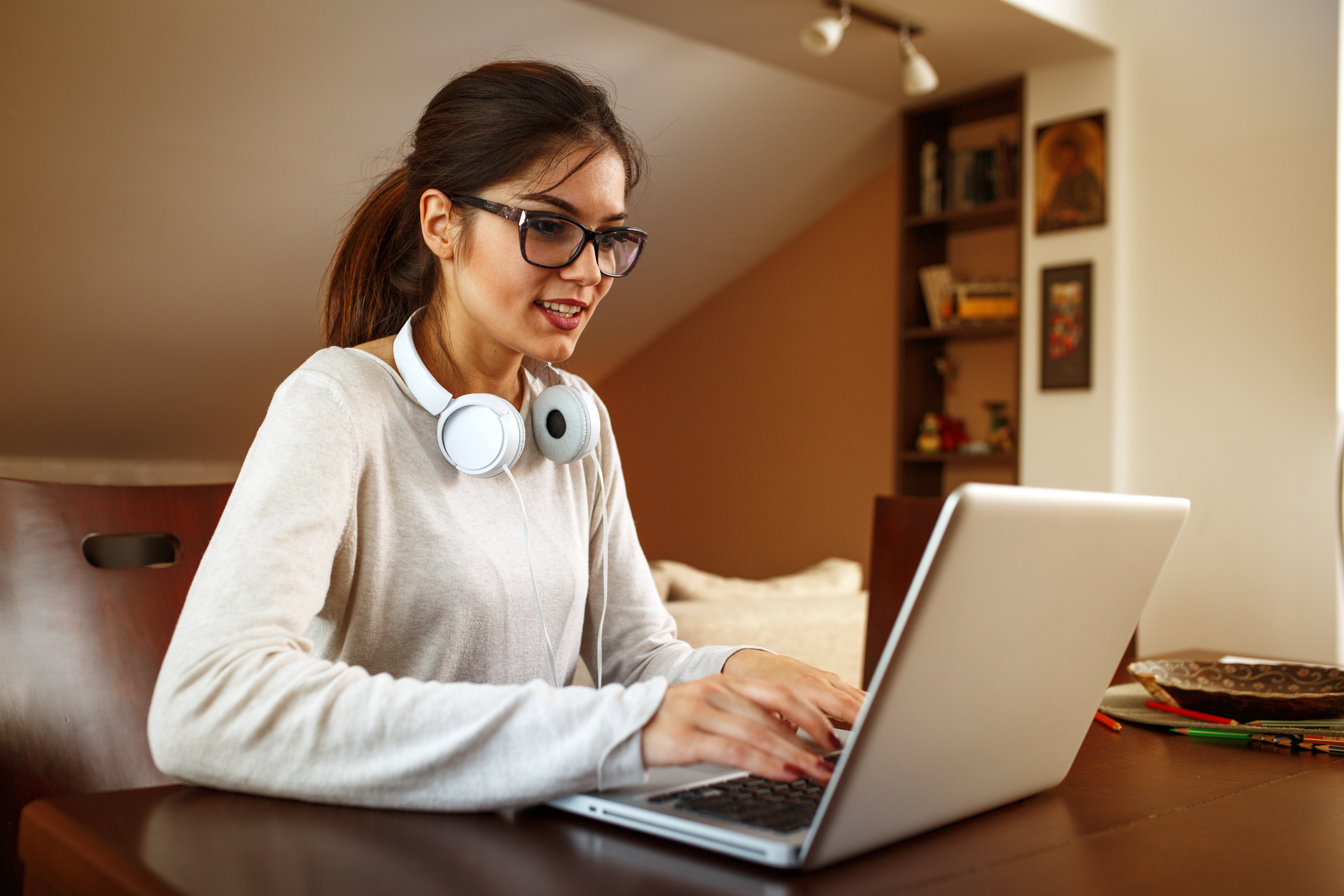 Student sitting at a desk using laptop with headphones, attending remote classes in a living room