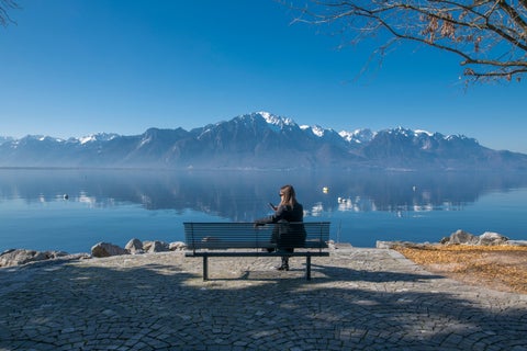 Tourist relaxing at a lakeside beach on Lake Geneva in Montreux, Switzerland, with the Alps mountains in the background