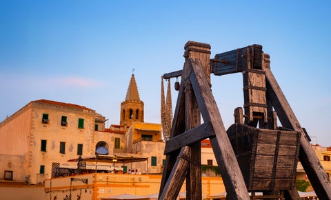 Wood artefact named 'Trabuccu Frame' with historic building in the background in Alghero, Italy