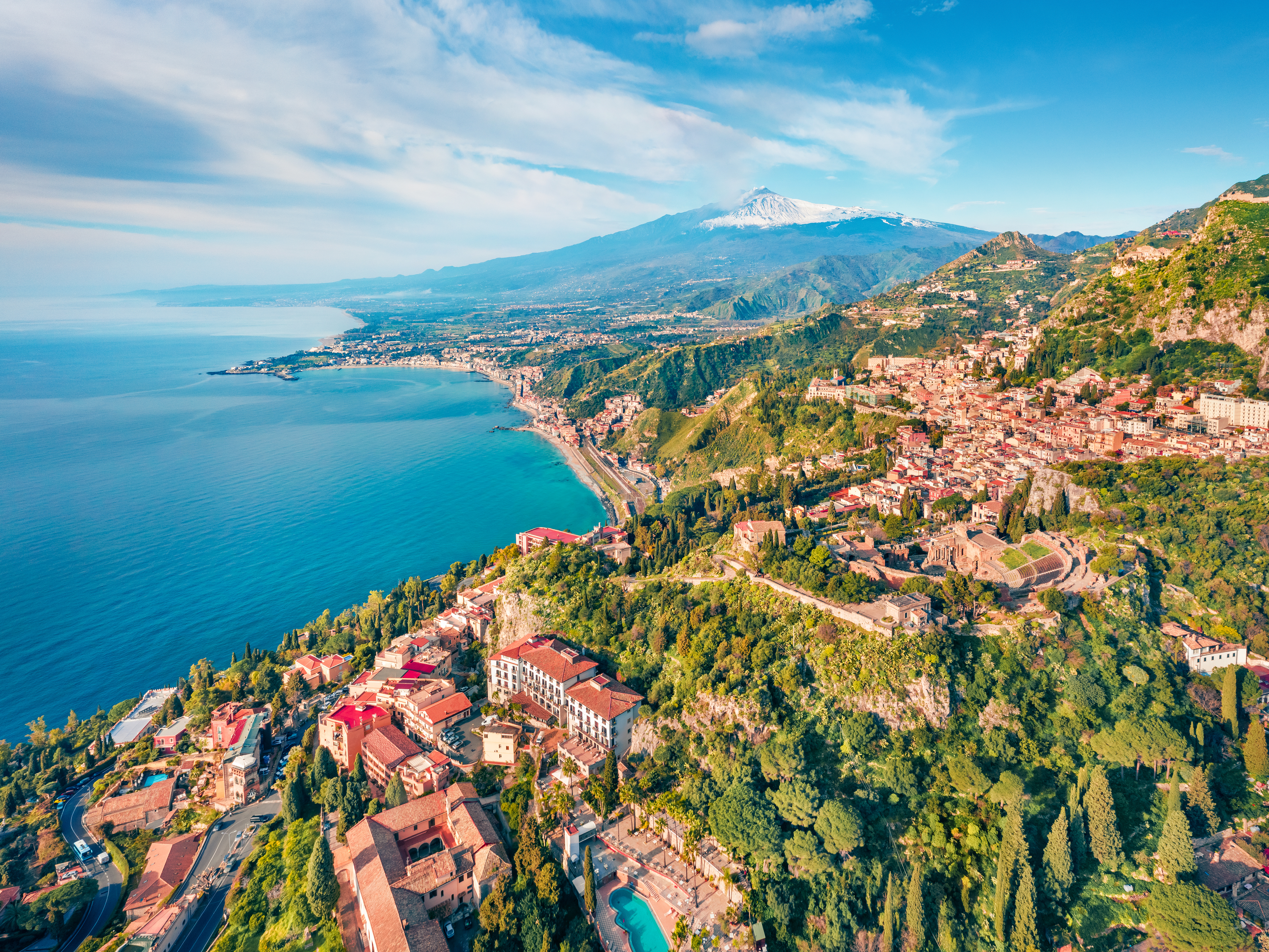 Aerial view of Taormina, Italy, with seaside houses on the hillside and Mount Etna in the background