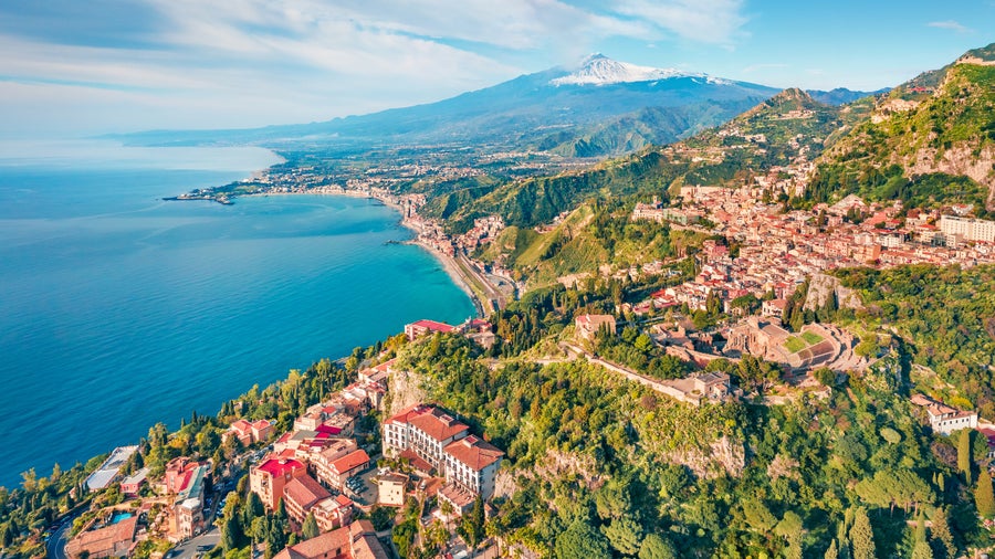 Aerial view of Taormina, Italy, with seaside houses on the hillside and Mount Etna in the background