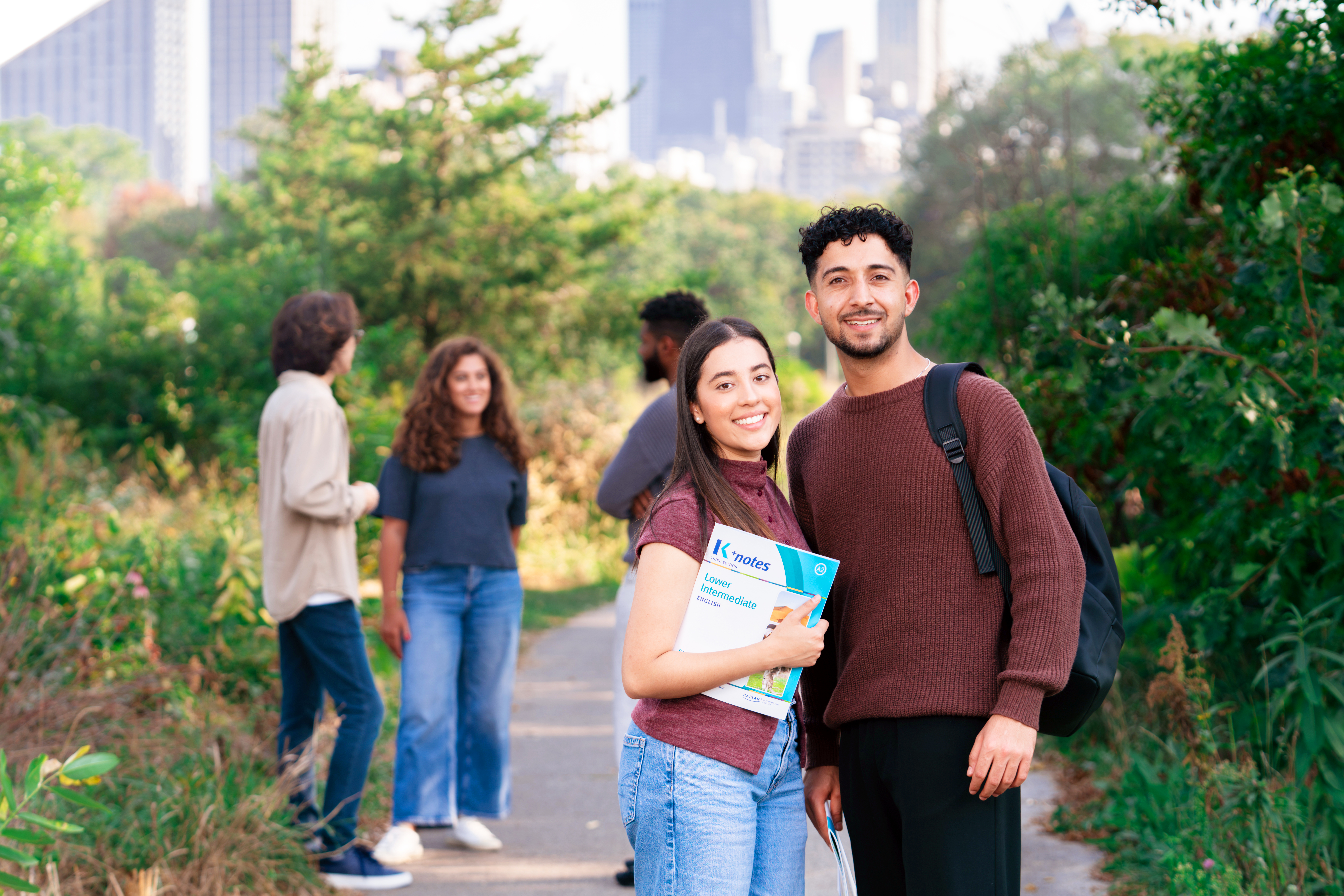 Students chatting and posing on the grass in a Chicago park with Kaplan folders