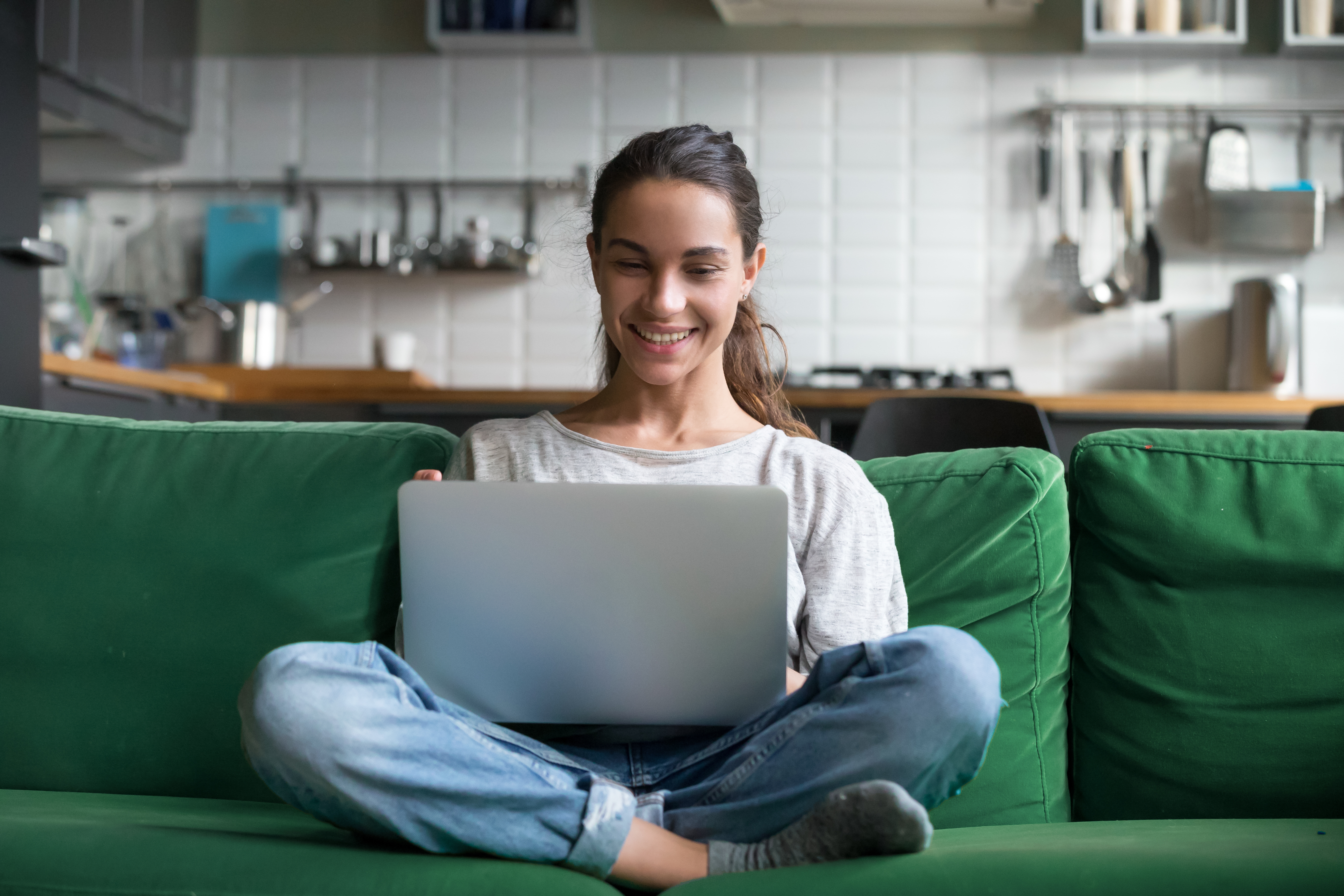 Young girl student taking remote classes at home, sitting on the sofa with a laptop during online learning