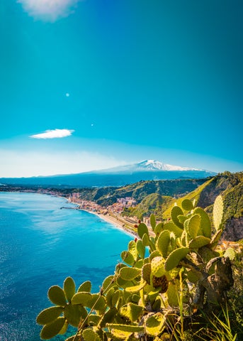 Aerial view of Taormina, Italy, with seaside houses on the hillside and Mount Etna in the background