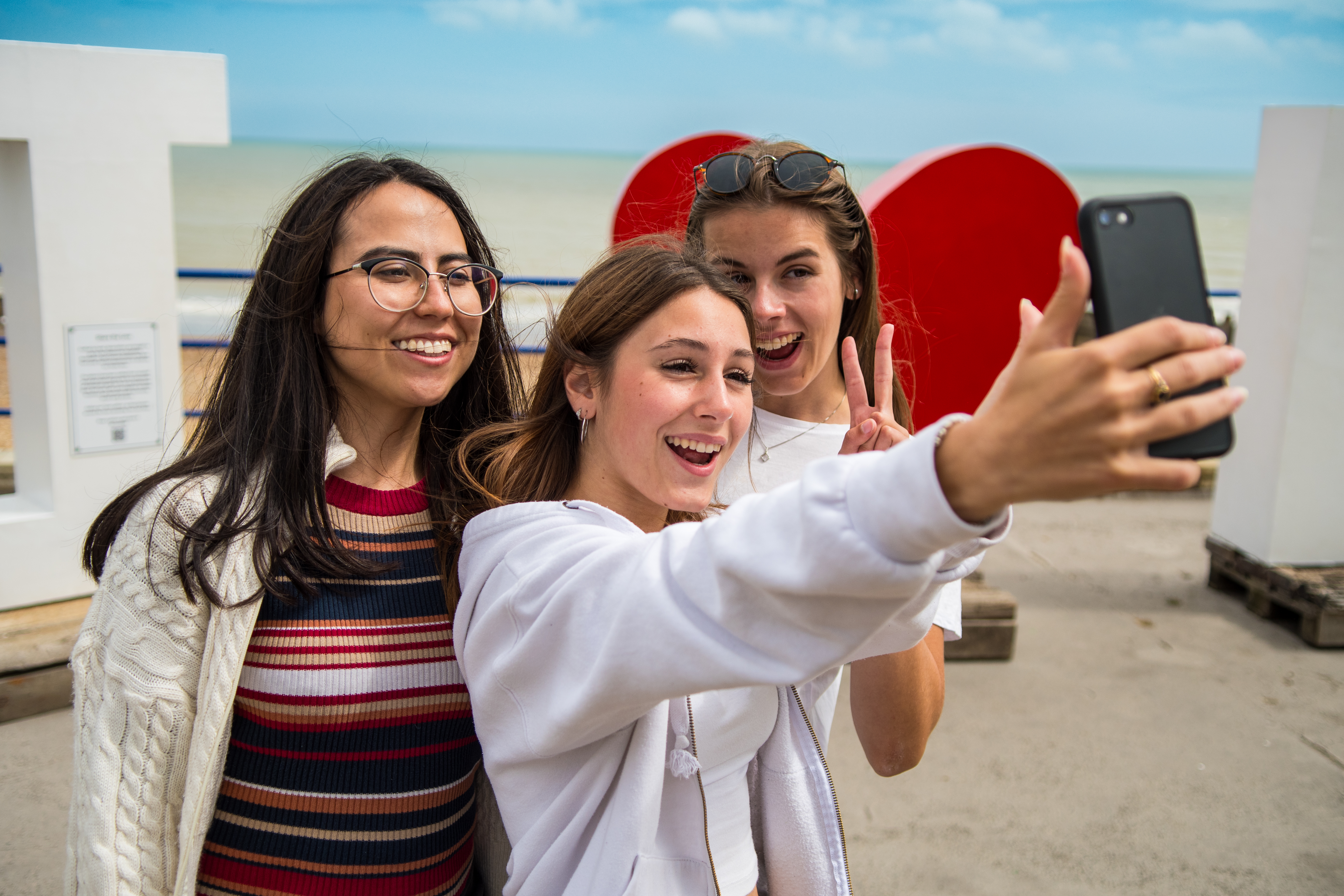 Three students taking a photo in front of the Eastbourne sign